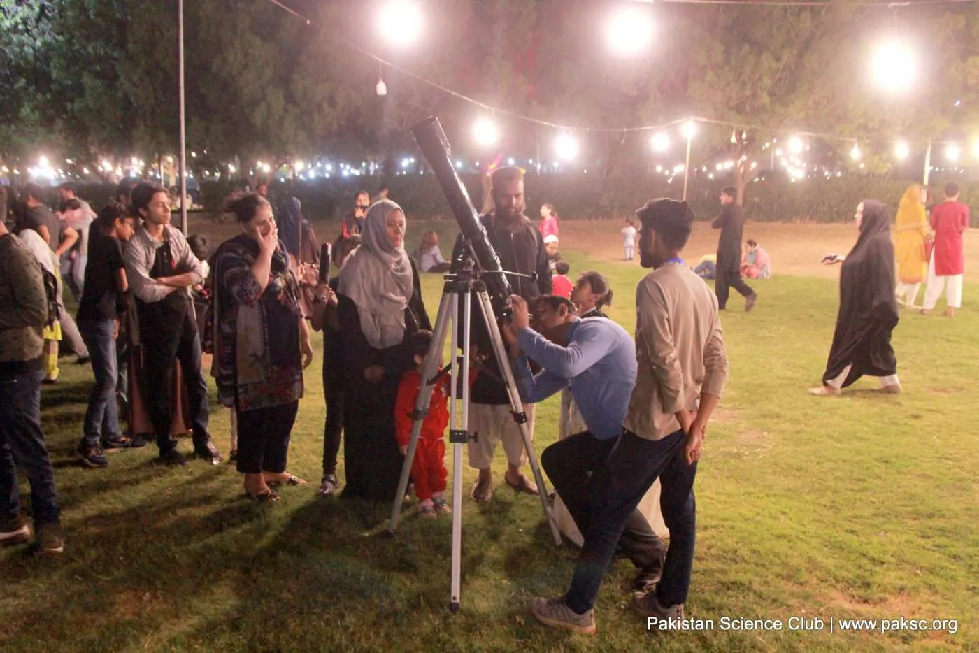 A volunteer adjusts a telescope on a tripod for a group of visitors on the lit lawn at Dream World Resort.