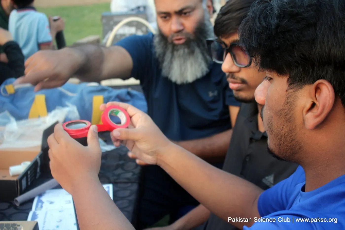 A teenager holds up the small red telescope he has just built while an instructor explains the lenses.